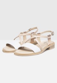 Sandali bianchi e beige con tacco piatto, cinturini incrociati e fibbia alla caviglia. Texture in pelle liscia con design minimalista.