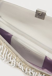 Ασημένια δερμάτινη τσάντα χειρός με λαμπερό ασημένιο κούμπωμα, μοβ επένδυση εσωτερικά και διακοσμητικό κρόσσι από μεταλλικές χάντρες και πλαστικά στοιχεία στη βάση.