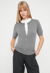 Svetlo siva kratka doza iz mehkih materialov, z okroglim ovratnikom, zapenjanjem spredaj na gumbe in rebrastim robom.