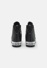 Zapatillas altas impermeables negras con acentos blancos, que cuentan con el logo de Chuck Taylor, suela de goma y costuras contrastantes en la parte posterior.