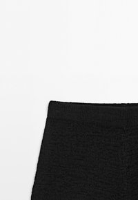Close-up of the upper section of black textured fabric pants with an elastic waistband, shown against a plain white background.