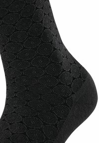 Schwarze Socken mit einem strukturierten Muster aus überlappenden Ovale. Der Stoff wirkt glatt mit einem leichten Glanz, der die dunkle Farbe betont.