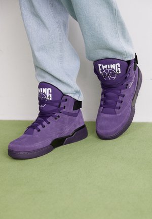 Fialové vysoké tenisky vyrobené z nubuku s černými akcenty, které mají robustní podešev, šněrování na přední straně a značkový jazyk.