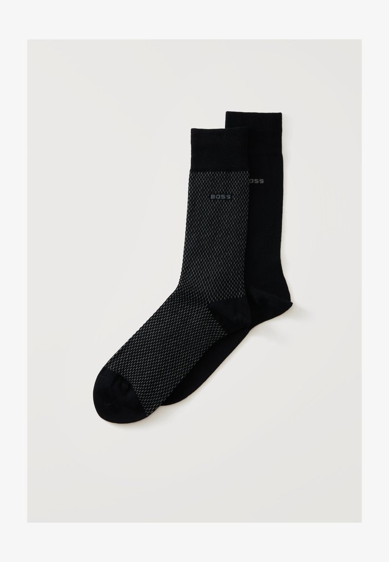 Paire de chaussettes habillées noires, une avec un petit motif gris et le logo "BOSS", l'autre noire unie avec un logo discret sur fond blanc uni.
