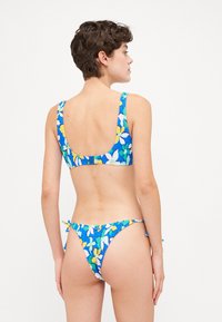 Bikini-setti, jossa on sininen kukkakuosi keltaisilla ja valkoisilla yksityiskohdilla. Yläosa on leveillä olkaimilla, kun taas alaosa on matalavyötäröinen malli nauhoilla.