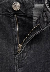 Črne denim hlače z vidnim kovinskim zadrgo, srebrnim gumbom in teksturirano tkanino, ki je nekoliko obrabljena v predelu zadrge.