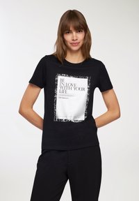 T-shirt in cotone nero con una grafica centrata che riporta il testo "AMA LA TUA VITA" in bianco e un bordo rettangolare in stile usurato.