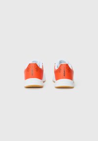 Red and white athletic shoes, featuring a textured orange heel, rounded shape, and rubber sole with visible grip patterns.