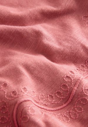Roosa kangas, millel on õrn tekstuur ja delikaatsed tikandid ühel serval, näidates pehmet ja siledat välimust.