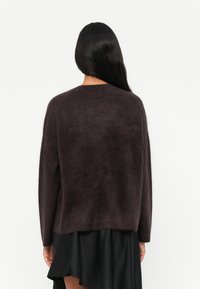 Maglione a maglia bordeaux con una vestibilità ampia, texture morbida e maniche lunghe. Si ferma in vita, abbinato a una gonna nera a strati.