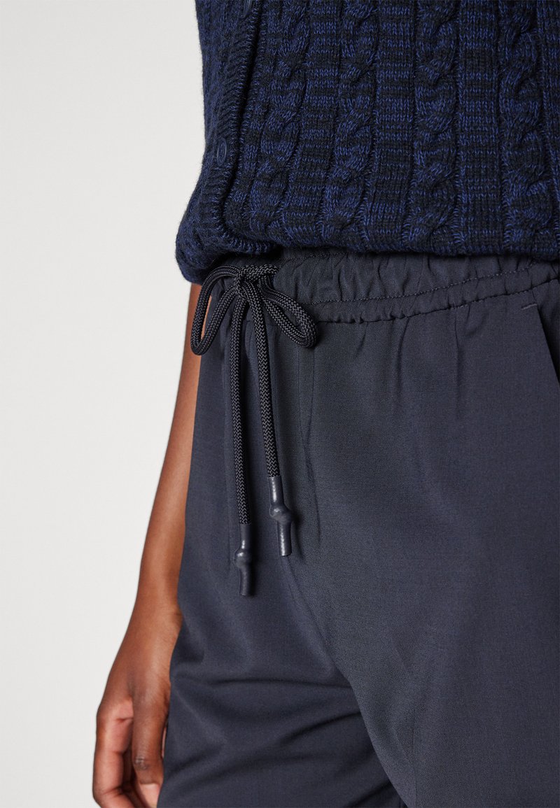 Granatowy bawełniany sweter z teksturą w splot warkoczowy, zestawiony z czarnymi spodniami na elastyczny pasek z troczkami i trokami.