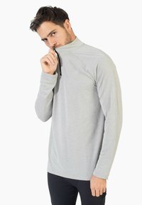 Camisa de manga larga gris claro con cuello alto y media cremallera. Presenta un patrón texturizado en toda la prenda y mangas ajustadas.