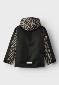 Schwarze Jacke mit einem Zebra-Muster an Kapuze und Ärmeln. Hat eine lockere Passform, einen hohen Kragen und ein kleines Logo-Patch near dem Saum.