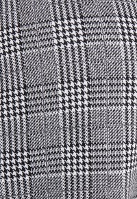 Svart och vit hundtandstyg med ett rutmönster som har varierande texturer och vävningar, vilket skapar djup och visuell intresse.