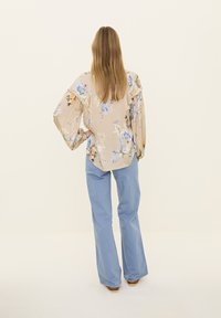 Blouse à motif floral en beige avec des manches froncées, associée à un pantalon évasé bleu clair. Texture douce et design fluide.