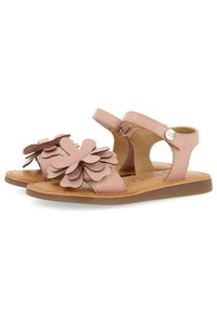 Roze leren sandalen hebben gelaagde bloem appliqués aan de voorkant, een verstelbare enkelband en een platte bruine zool.