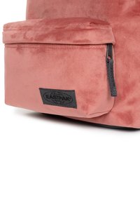 Zaino in velluto rosa con tasca frontale con zip; presenta un patch del logo Eastpak nero e una superficie testurizzata. Design compatto, materiale morbido.