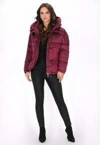 Bordó színű steppelt dzseki kapucnival, cipzáras lezárással, elasztikus mandzsettákkal és oldalzsebekkel; fekete, testhez simuló nadrággal és bokacsizmával párosítva.