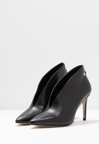 Bottines en cuir noir à bout pointu avec talon, design ajouré, ornées d'un petit accent doré sur le côté et d'un talon stiletto.