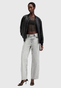 Chaqueta bomber de cuero negro sobre un top corto transparente con lunares, combinada con jeans de pierna ancha de tiro alto y gris deslavado, y tacones negros con tiras.