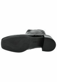 Bottine en cuir noir avec une semelle en caoutchouc texturée à motif zigzag, un talon carré et un design supérieur lisse.