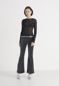 Schwarze, durchsichtige Bluse mit langen Ärmeln und silbernen Punkten, kombiniert mit schwarzen, weit geschnittenen Hosen, akzentuiert durch einen metallischen Gürtel und glänzenden silbernen Stiefeln.