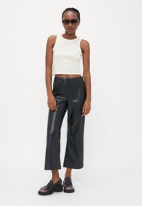 Tætsiddende hvid crop top, højtskåret sorte faux læderbukser og sorte platform loafers med lilla accent, båret med mørke solbriller.
