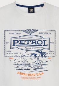 Bílá bavlněná tričko s modrým potiskem. Text obsahuje "PETROL," palmy, hory a vozidlo. Kulatý výstřih.