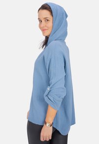 Hellblauer, strukturierter Hoodie mit einer Fronttasche, hochgekrempelten Ärmeln und einer lässigen Passform. Hergestellt aus einem weichen, atmungsaktiven Stoff.