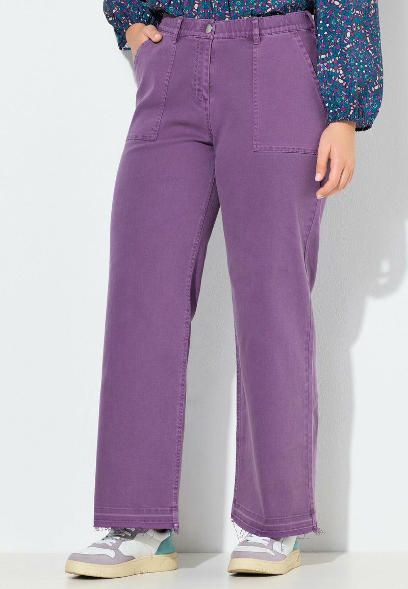 Jeans morados de pierna ancha con cintura alta, que presentan grandes bolsillos frontales y un dobladillo desflecado. Combinados con zapatillas multicolor.