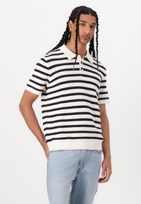 Stribet kortærmet polo shirt i creme og marineblå. Har krave, knaplukning, ribbede kanter og struktureret strikstof.