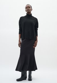 Maglione nero a collo alto abbinato a una gonna nera a campana, entrambi realizzati in tessuto morbido. Il look è completato da stivali neri alti fino al ginocchio.