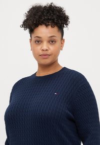 Tummansininen neulepaita, jossa on tekstuurikuvio, pyöreä pääntie ja pieni logo korostus rinnassa. Pehmeä ja mukava kangas.