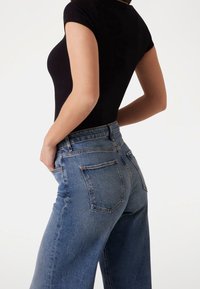 Černý žebrovaný bodysuit s krátkým rukávem v kombinaci s vysokým pasem a volnými světle modrými džíny, které mají čtyři zadní kapsy.