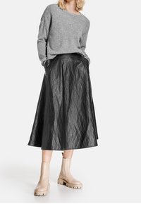 Grå stickad tröja med bred halsringning, kombinerad med en svart, knälång, texturerad kjol. Beiga ankelstövlar med en kraftig sula.