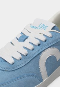 Ανοιχτό μπλε σουέντ αθλητικό παπούτσι με λευκά κορδόνια και σόλα, με λευκό σχέδιο σε σχήμα καρδιάς και το κείμενο "LOVE" στη γλώσσα του παπουτσιού.