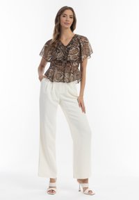 Brun og beige slangeskindsprint peplum bluse med flæseærmer, parret med højtaljede hvide bukser og nude højhælede sandaler.