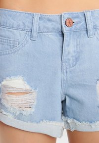 Světle modré džíny šortky s vybledlými dírami, třepeným lemem a zapínáním na knoflík. Obsahují přední kapsy a prošívané detaily.