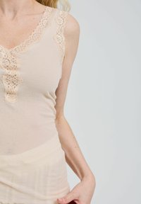 Beige Trägershirt mit Spitzenbesatz am Halsausschnitt und dekorativen Knöpfen. Der Stoff hat eine weiche, glatte Textur und eine figurbetonte Passform.