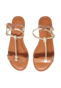 Sandali finti in pelle color tan con una cinghia texturizzata, un sottile accento metallico e un design minimalista. La suola è piatta e liscia.