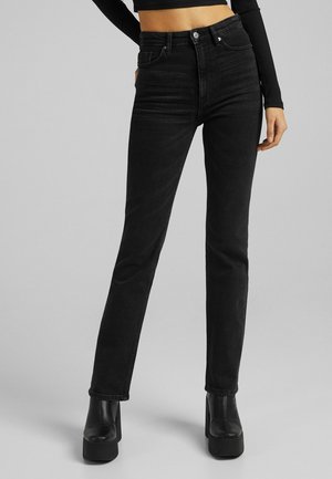Black high-waisted jeans made of denim, slim fit, with contrast stitching and a five-pocket design, paired with chunky black platform boots.