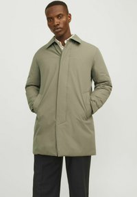 Chaqueta verde claro de longitud media con un cuello puntiagudo y dos bolsillos frontales, que presenta un acabado liso y mate.
