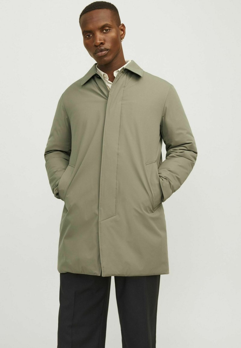 Chaqueta verde claro de longitud media con un cuello puntiagudo y dos bolsillos frontales, que presenta un acabado liso y mate.