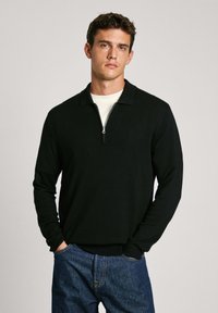 Schwarzer Reißverschluss-Pullover mit kragen, gerippten Bündchen und Saum, kombiniert mit blauen Denim-Jeans. Glatte Textur, lässiges Design.