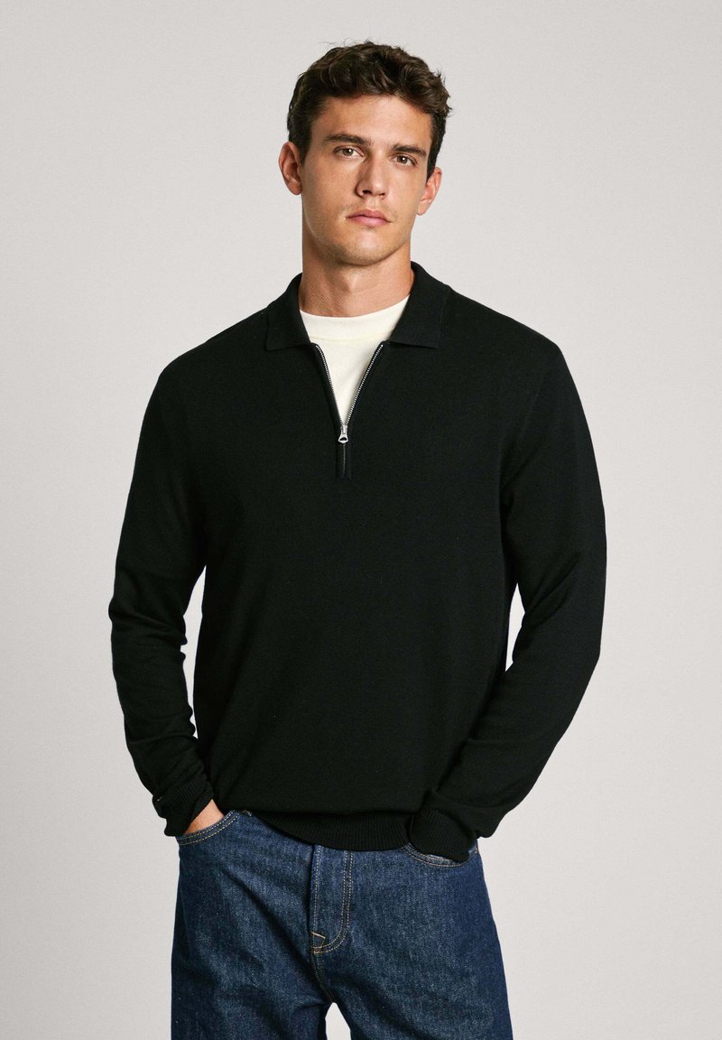 Schwarzer Reißverschluss-Pullover mit kragen, gerippten Bündchen und Saum, kombiniert mit blauen Denim-Jeans. Glatte Textur, lässiges Design.