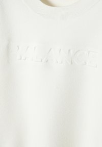 Felpa bianca con collo a costine e testo in rilievo "BALANCE" sulla parte anteriore. Texture morbida, design minimalista e nessun motivo visibile.