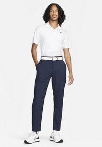White short-sleeve polo with a collar and Nike logo, paired with navy trousers featuring a belt with a white buckle and black accents.