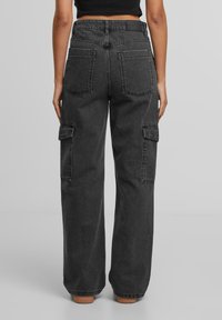 Pantalons cargo en denim noir avec une coupe décontractée, dotés de poches latérales et d'une taille haute. Le tissu a une apparence douce et texturée.