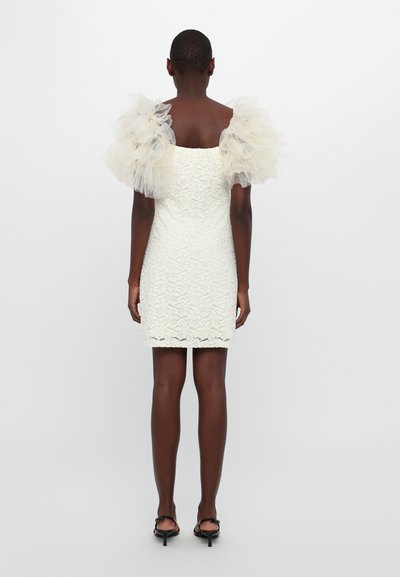 Korte witte kantjurk met doorschijnende, puffy tule mouwen. De stof is gestructureerd, aansluitend, met een rechte silhouet en een lengte boven de knie.