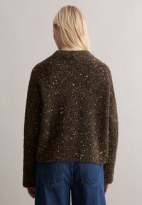 Brązowy dziany sweter z wielokolorowymi kropkami, z zaokrąglonym dekoltem i luźnym krojem. Tekstura wydaje się miękka i gruba.